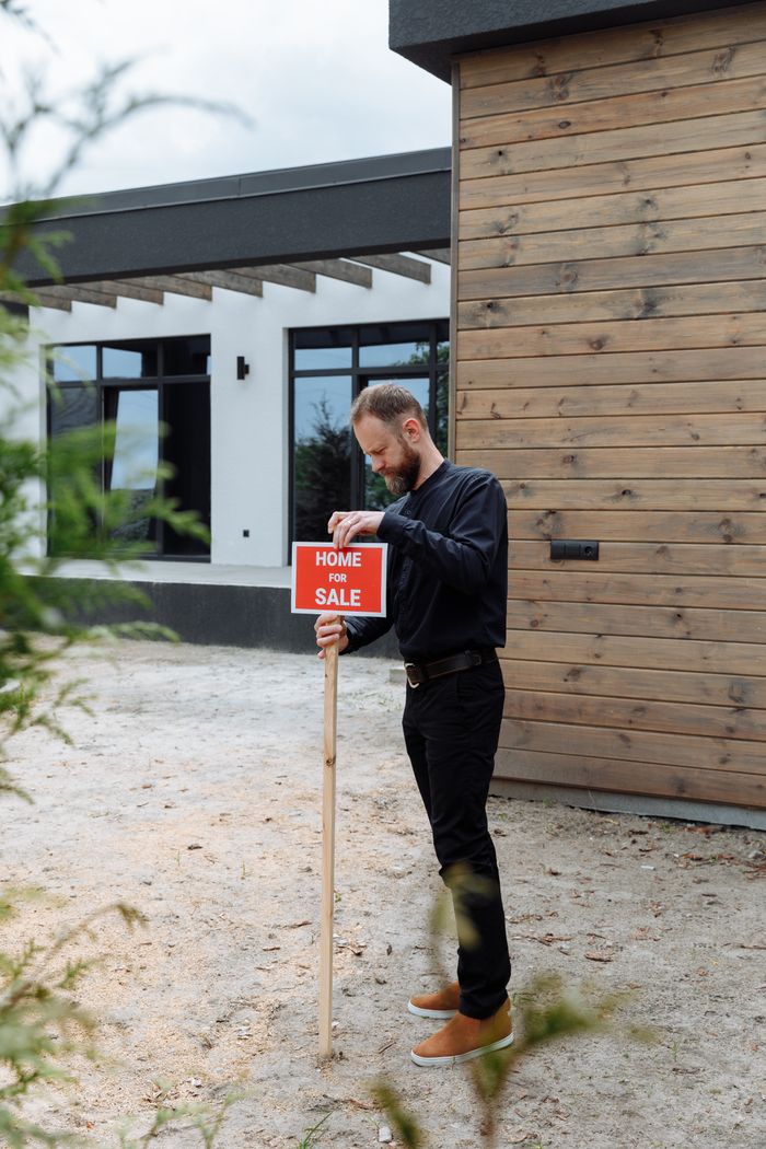 A real estate agent holding a home for sale sign in front of a modern house.